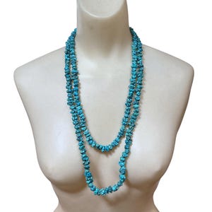 Puede incluir: Un collar largo de doble hebra que presenta numerosas piedras peque&ntilde;as, irregulares y pulidas de color turquesa con vetas de matriz oscura. Las cuentas est&aacute;n ensartadas en un bucle continuo, creando una apariencia de capas alrededor del cuello.
