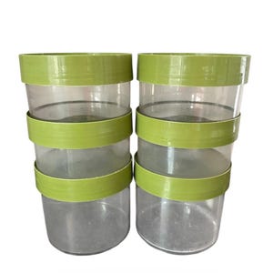 Puede incluir: Dos juegos de recipientes cilíndricos transparentes con bandas verde brillante. Cada juego tiene tres recipientes apilados uno encima del otro. Los recipientes son de plástico transparente y están vacíos.