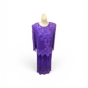 May include: A vibrant purple two-piece set consisting of a long-sleeved top and a matching skirt. The entire ensemble is heavily embellished with intricate beadwork and sequins, featuring floral patterns and scalloped edges on the hemline.