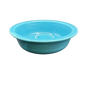 May include: A turquoise ceramic bowl with a wide, shallow design. The bowl has a smooth, glossy finish and a slightly flared rim. The interior of the bowl is a lighter shade of turquoise.