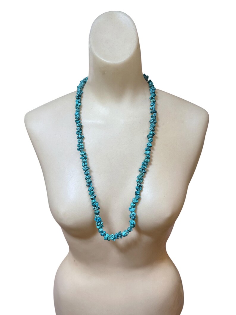 Puede incluir: Un collar largo compuesto por numerosas piedras peque&ntilde;as, irregulares y pulidas de color turquesa. Las cuentas presentan un tono azul verdoso vibrante con patrones de matriz oscuros similares a una red, ensartadas en una sola hebra.