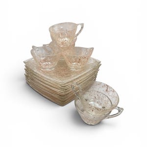 May include: A collection of clear glass teacups and saucers featuring a subtle, crackled design in brown tones. The cups have handles and rest on square saucers, neatly stacked. The glassware is suitable for serving tea.