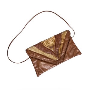 May include: Brown leather clutch with a long strap. The flap features a geometric design with gold and brown snake-print accents. The bag is a triangular shape.