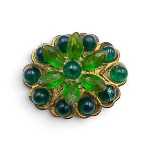 May include: A circular brooch featuring a central cluster of faceted, light green marquise-shaped stones surrounded by a ring of dark green, smooth, round cabochon stones set in a textured, antiqued gold-tone metal base with scalloped edges.