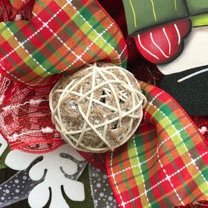 May include: A Christmas wreath with red and green plaid ribbon, a white snowflake, and a brown and white ball ornament.