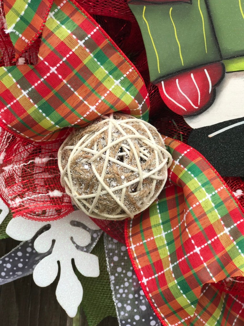 May include: A Christmas wreath with red and green plaid ribbon, a white snowflake, and a brown and white ball ornament.