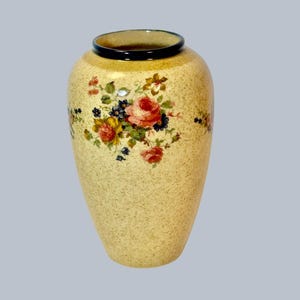 May include: A cream-coloured ceramic vase with a floral pattern. The vase has a dark blue rim and features pink, yellow, and blue flowers.