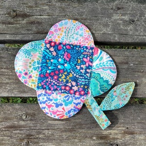 Pu&ograve; includere: Un fiore di stoffa colorato con un motivo floreale blu, rosa e verde. Il fiore &egrave; composto da pi&ugrave; pezzi di stoffa cuciti insieme.