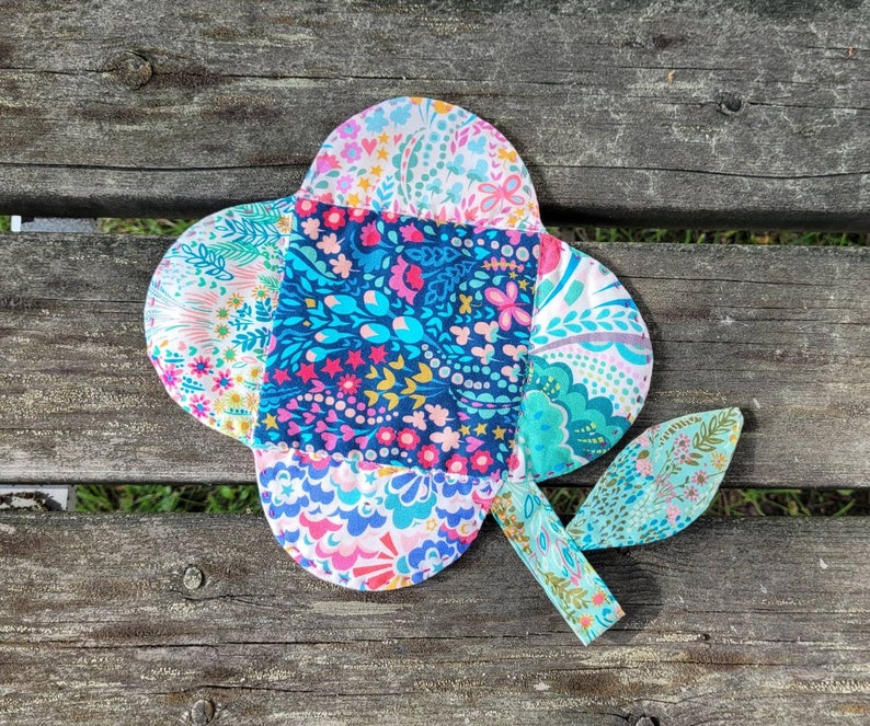 Pu&ograve; includere: Un fiore di stoffa colorato con un motivo floreale blu, rosa e verde. Il fiore &egrave; composto da pi&ugrave; pezzi di stoffa cuciti insieme.