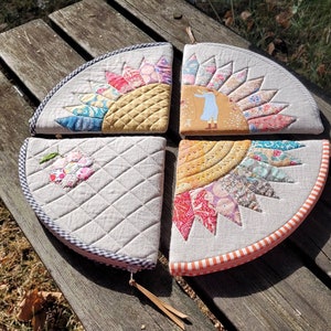 Puede incluir: Cuatro bolsas de tela acolchadas con diferentes diseños. Cada bolsa es un cuarto de círculo y tiene una cremallera. Los diseños incluyen una flor, un sol y una niña con un vestido.