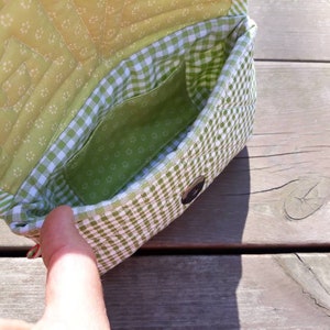May include: A small green and white checkered fabric purse with a green quilted lining. The purse has a small pocket on the inside.
