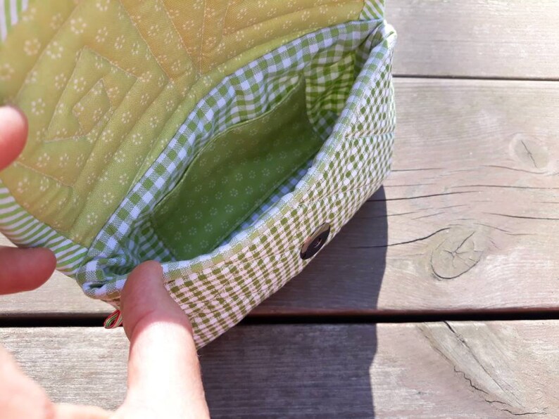 May include: A small green and white checkered fabric purse with a green quilted lining. The purse has a small pocket on the inside.