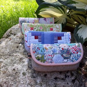 May include: Four quilted fabric pouches with different patterns. The pouches are stacked on top of each other on a gray rock. The pouches are made of patchwork fabric with a variety of colors and patterns.