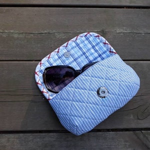 May include: A blue and white quilted fabric case with a snap closure. A pair of sunglasses is inside the case.