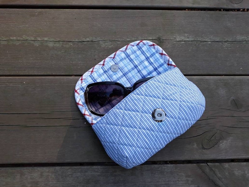 May include: A blue and white quilted fabric case with a snap closure. A pair of sunglasses is inside the case.