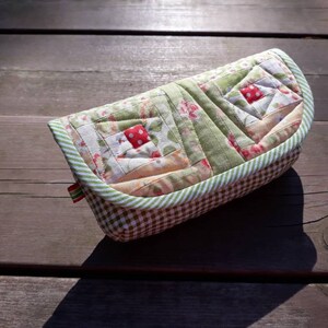 May include: A green and white quilted fabric case with a red and white floral pattern. The case has a gingham lining and a green and white striped trim.