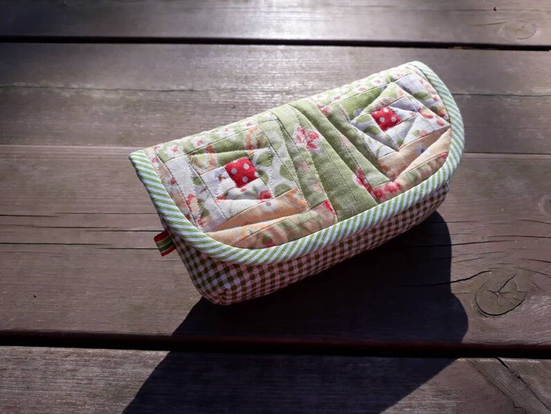 May include: A green and white quilted fabric case with a red and white floral pattern. The case has a gingham lining and a green and white striped trim.
