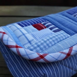 May include: A blue and white patchwork fabric clutch with a red and white plaid trim. The clutch is made from repurposed fabric and has a unique, handmade look.