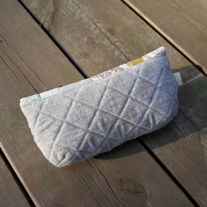 May include: A gray quilted zippered pouch with a floral patterned fabric lining. The pouch is lying on a wooden surface.