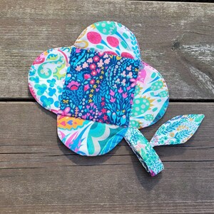 Pu&ograve; includere: Un fiore di stoffa colorato con un motivo floreale blu, verde, rosa e bianco. Il fiore ha una coda lunga e sottile che &egrave; anche ricoperta di stoffa.