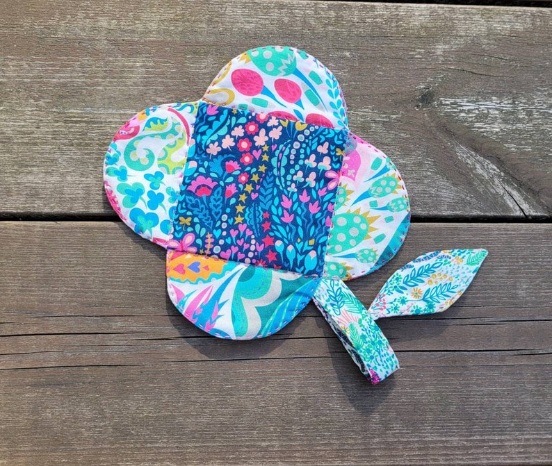 Pu&ograve; includere: Un fiore di stoffa colorato con un motivo floreale blu, verde, rosa e bianco. Il fiore ha una coda lunga e sottile che &egrave; anche ricoperta di stoffa.