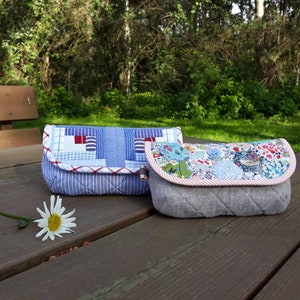 May include: Two fabric pouches, one with a blue and white patchwork design and the other with a floral print, are sitting on a wooden table.