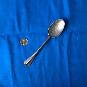 May include: A silver spoon on a blue fabric background. A silver coin is also visible in the image.