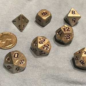 May include: A collection of metallic dice in various shapes, including a four-sided die, a six-sided die, an eight-sided die, a ten-sided die, a twelve-sided die, and a twenty-sided die. A U.S. quarter is included for size comparison.