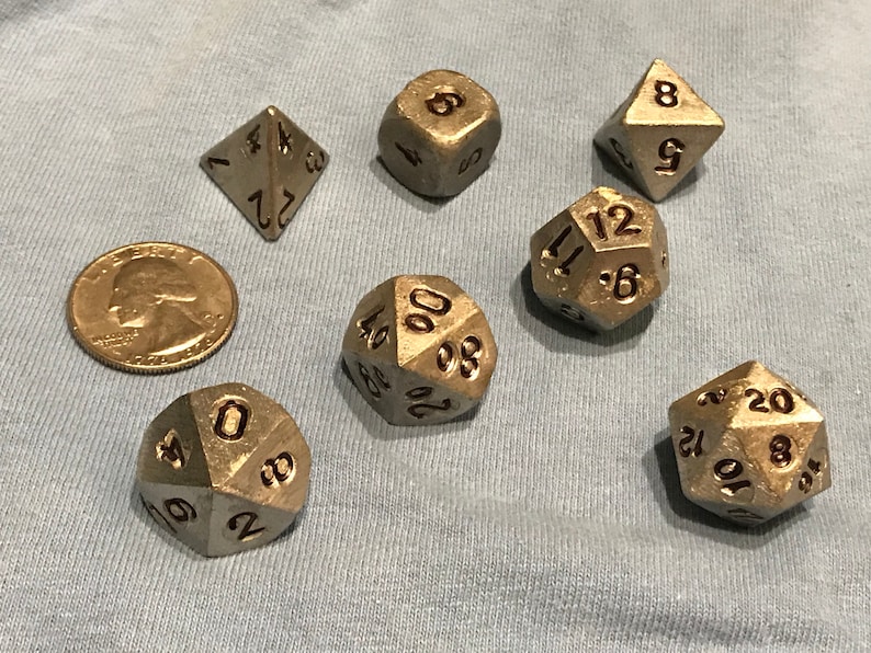 May include: A collection of metallic dice in various shapes, including a four-sided die, a six-sided die, an eight-sided die, a ten-sided die, a twelve-sided die, and a twenty-sided die. A U.S. quarter is included for size comparison.