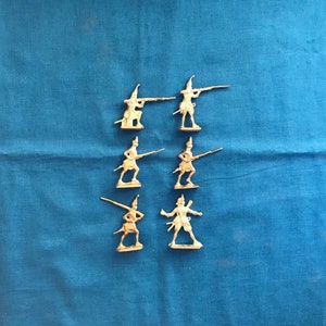 May include: Six miniature toy soldiers made of metal, painted in a light brown colour. The soldiers are holding rifles and are posed in a standing position.