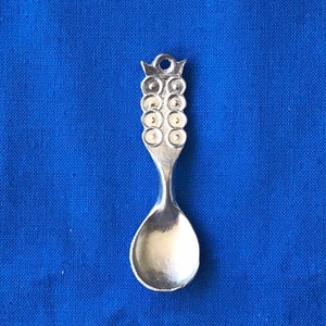 May include: A silver spoon with a decorative handle featuring a series of circles. The spoon is on a blue background.