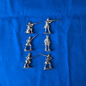May include: Six silver toy soldiers standing in a row on a blue background. The soldiers are holding rifles and are dressed in military uniforms.