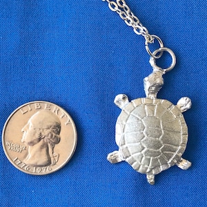 May include: Silver turtle pendant necklace with a chain. The turtle is about the size of a UK 20 pence coin.