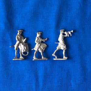 May include: Three silver toy soldiers, one playing a drum, one playing a bugle, and one holding a flag. The soldiers are standing on a blue surface.