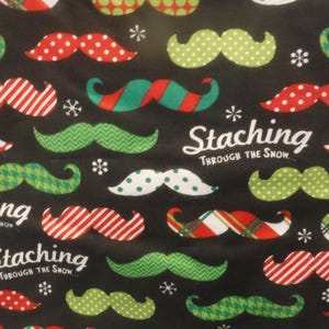 May include: Black fabric with a repeating pattern of festive mustaches in red, green, and white. The mustaches have various designs, including polka dots, stripes, and zigzags. The text "Staching Through The Snow" is also present.