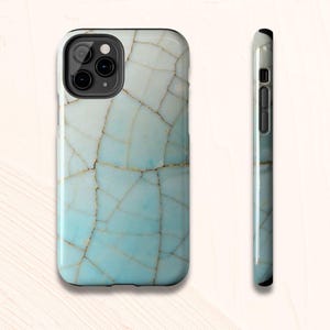 May include: A smartphone case with a cracked, mosaic-like design in shades of light blue and white. The case has a glossy finish and a black border. The side view shows the case's slim profile and button placement.