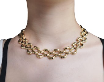 Könnte beinhalten: Eine goldfarbene Halskette mit einem klobigen, mehrlagigen Kettendesign. Die Halskette besteht aus ineinandergreifenden, gebogenen Gliedern, die einen einzigartigen und auffälligen Look erzeugen.