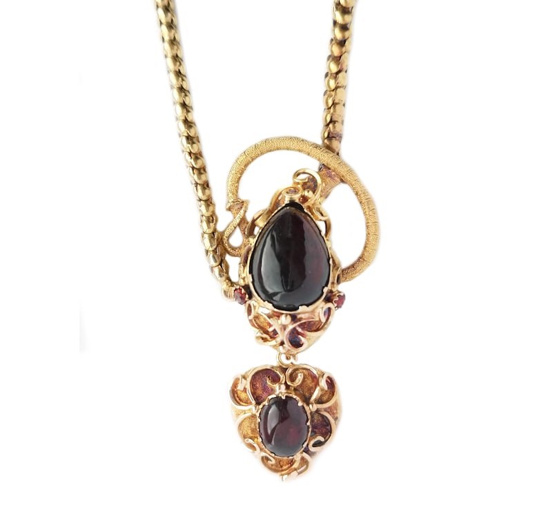 May include: A gold necklace with a pendant featuring two dark red gemstones set in intricate gold filigree. The pendant is shaped like a teardrop and a heart.
