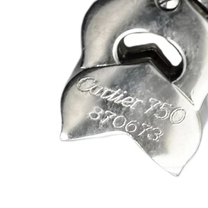 May include: Close-up of a silver Cartier bracelet with the inscription 'Cartier 750 870673'.
