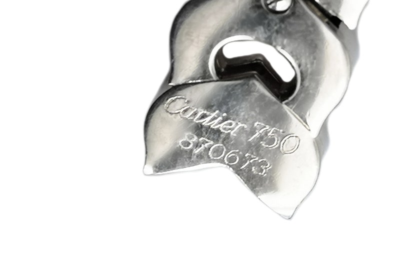 May include: Close-up of a silver Cartier bracelet with the inscription 'Cartier 750 870673'.