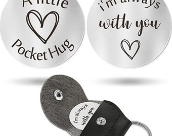 May include: Two silver pocket tokens with inspirational messages. One token reads "A little Pocket Hug" with a heart design. The other token reads "i'm always with you" with a heart design. The tokens are shown in a black leather keychain holder.
