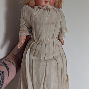 Alte, antike Puppe mit gruseligen Augen, weißer Kleidung, Kopf aus Kompositmaterial, Körper aus Stroh, gespenstisch und unheimlich.