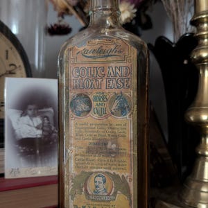 Peut inclure: Une bouteille en verre ambré vintage avec un corps rectangulaire et un goulot étroit. L'étiquette avant présente le texte Rawleigh's Colic and Bloat Ease for Horses and Cattle, ainsi que des illustrations de têtes de chevaux et un portrait.