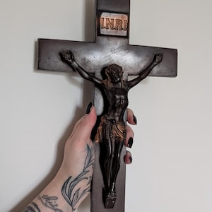 May include: A dark brown wooden crucifix with a bronze figure of Jesus. The cross features the letters INRI at the top. The figure is detailed with a draped cloth around the waist. A religious item.