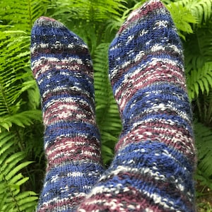 May include: A pair of blue, white, and burgundy striped knitted socks. The socks are made with a textured yarn and have a unique pattern.