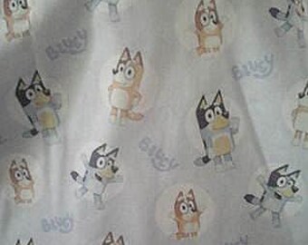 May include: White bib featuring a repeating pattern of cartoon dog characters in various poses. The bib has a rounded shape and is made of a soft, likely absorbent material. The word "Bluey" is printed on the bib.