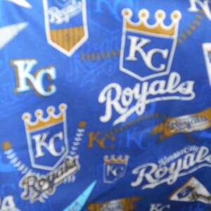 May include: Blue fabric with a repeating pattern of the Kansas City Royals logo. The logo features a crown, the letters "KC", and the word "Royals".