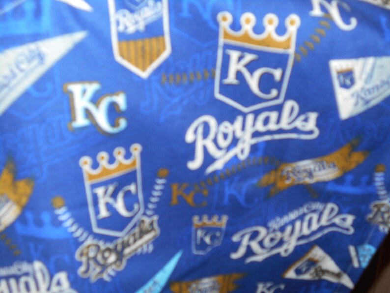 May include: Blue fabric with a repeating pattern of the Kansas City Royals logo. The logo features a crown, the letters "KC", and the word "Royals".