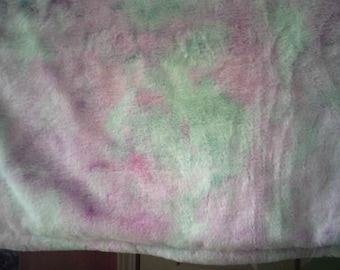 May include: A soft, plush blanket with a tie-dye pattern in shades of pink, green, and purple. The blanket has a fluffy texture and a subtle sheen, creating a cozy and inviting appearance. The colors blend together in a watercolor effect.