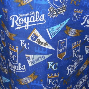 May include: A blue fabric with a repeating pattern of the Kansas City Royals logo. The logo features a crown, the letters "KC", and the word "Royals".